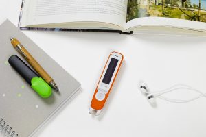 C-Pen Exam Reader 2 sul tavolo con: libro, auricolari e quaderno con sopra penna ed evidenziatore