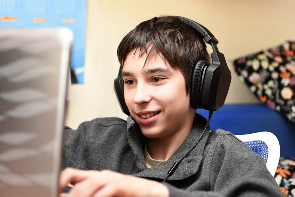 A boy wearing headphones to use text-to-speech while completing the tests on a laptop computer