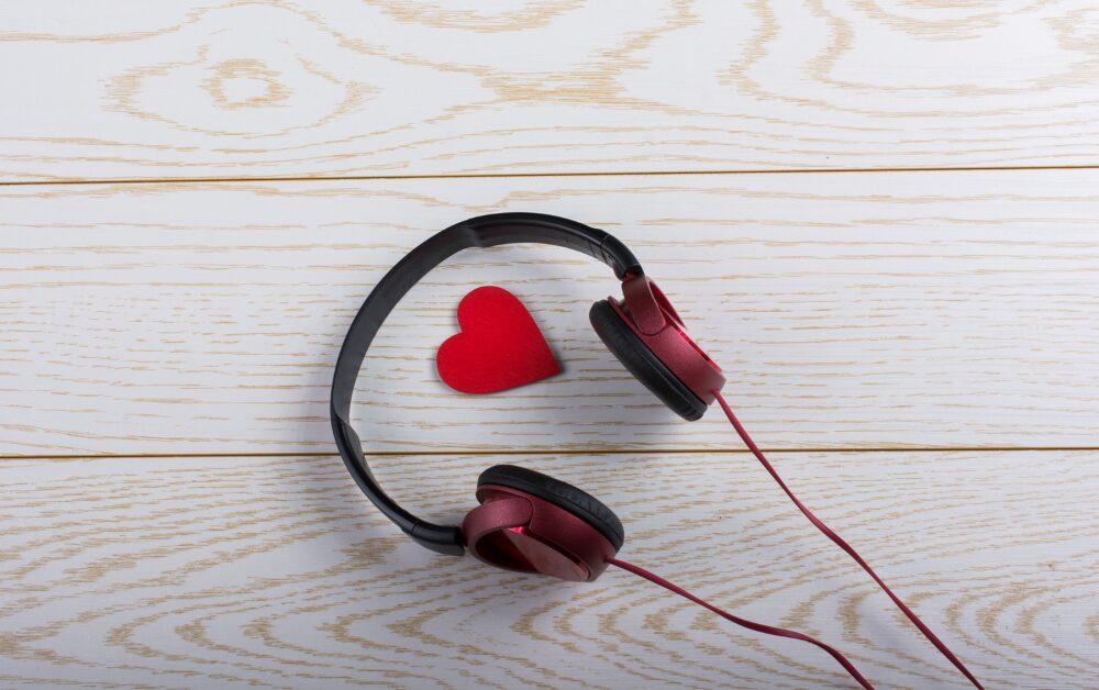 Cuffie audio bordeaux e nere posate su una superficie di legno chiaro, con un piccolo cuore rosso all'interno dell'archetto. L'immagine richiama l'ascolto e la cura, evocando strumenti come la sintesi vocale nell'ambito del supporto all'apprendimento.