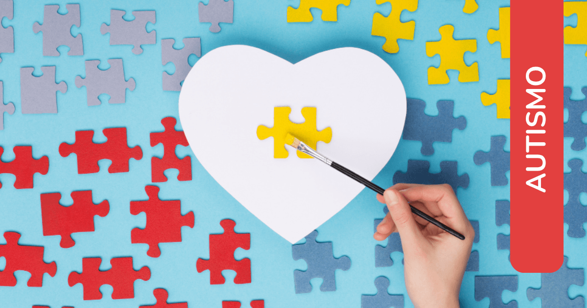 Mano che dipinge un pezzo di puzzle giallo su un cuore bianco, circondato da pezzi colorati. Etichetta: "Autismo".