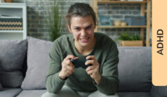 Ragazzo adolescente seduto sul divano di casa con un'espressione di intensa concentrazione, che stringe un controller da videogioco con le mani