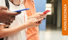 Dettaglio di vari adolescenti affiancati che guardano gli smartphone, in piedi in un corridoio scolastico