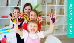 Dei bambini sorridenti insieme alla maestra della scuola d'infanzia alzano le mani con cui hanno appena dipinto con i colori a dita