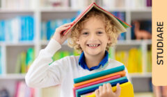 Un bambino sorridente davanti ad una libreria con un libro aperto appoggiato sulla testa a mo' di cappello