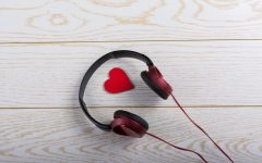 Cuffie audio bordeaux e nere posate su una superficie di legno chiaro, con un piccolo cuore rosso all'interno dell'archetto. L'immagine richiama l'ascolto e la cura, evocando strumenti come la sintesi vocale nell'ambito del supporto all'apprendimento.