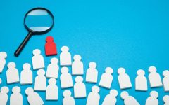 Gruppo di sagome stilizzate bianche su sfondo azzurro, tra cui spicca una figura rossa. Una lente di ingrandimento posta sopra di essa ne evidenzia la diversità rispetto alle altre, evocando il concetto di identificazione, diagnosi o individuazione di una caratteristica specifica in mezzo a un gruppo.