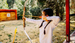 Ragazzina che tende un arco focalizzando al massimo la sua attenzione