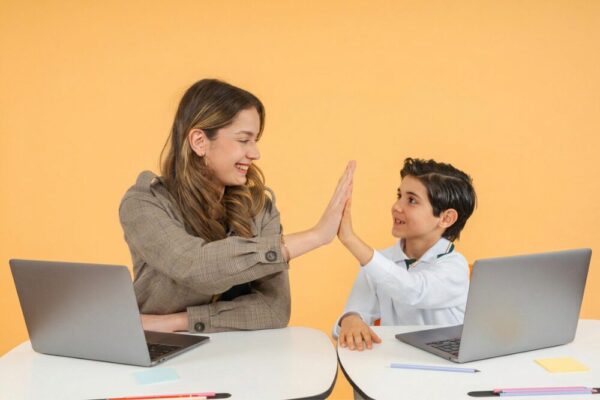 Insegnante e bambino si danno il cinque sorridendo, seduti ai rispettivi laptop su sfondo arancione.