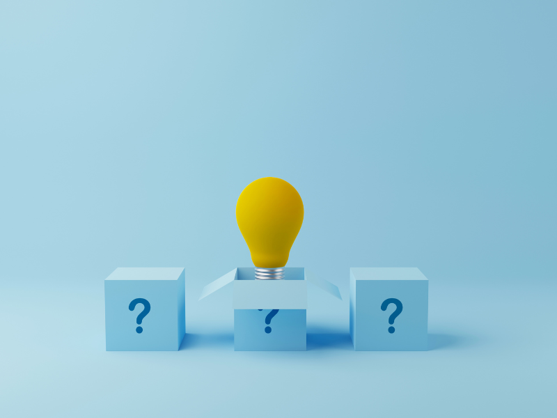 Tre cubi azzurri su sfondo azzurro, ciascuno con un punto interrogativo blu. Dal cubo centrale si apre un coperchio a forma di frecce divergenti, da cui emerge una lampadina gialla, simbolo di un'idea o di una risposta che emerge dall'incertezza.