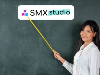 Insegnante sorridente davanti a una lavagna che indica con un puntatore il logo di SMX Studio.