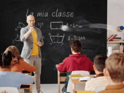 Insegnante davanti a una lavagna con scritto "La mia classe" e formule geometriche, con alunni seduti ai banchi.